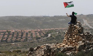 A Palestinian waves a flag in front of the W. Bank Jewish settlement of Ofra, April 26, 2013.