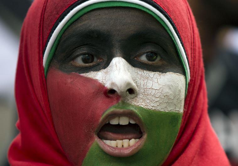 A protester with her face painted in the colors of the Palestinian flag chants in London