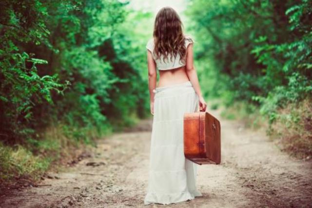 Young woman with suitcase in hand going away by a rural road (photo credit: INGIMAGE)