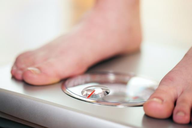 Woman standing on bathroom scale measuring her weight  (photo credit: INGIMAGE)