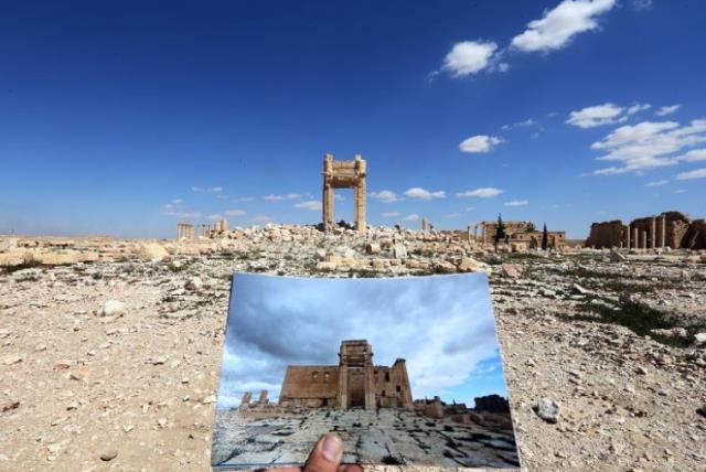 A general view taken on March 31, 2016 shows a photographer holding his picture of the Temple of Bel taken on March 14, 2014 in front of the remains of the historic temple after it was destroyed by Islamic State (photo credit: AFP PHOTO)