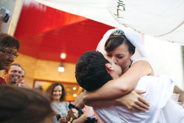 A bride and groom kiss under the chuppah at their wedding (photo credit: NIR ELIAS / REUTERS)