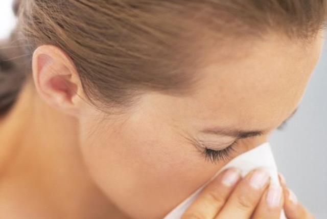 A woman blowing her nose into a tissue, possibly after sneeze or while sick (photo credit: INGIMAGE)