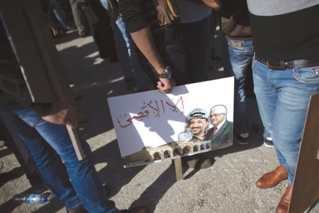 PALESTINIANS STAND next to a portrait of the Palestinian Authority President Mahmoud Abbas and the late Palestinian leader Yasser Arafat during a rally marking the tenth anniversary of Arafat’s death in Ramallah in 2014. ( (photo credit: REUTERS)