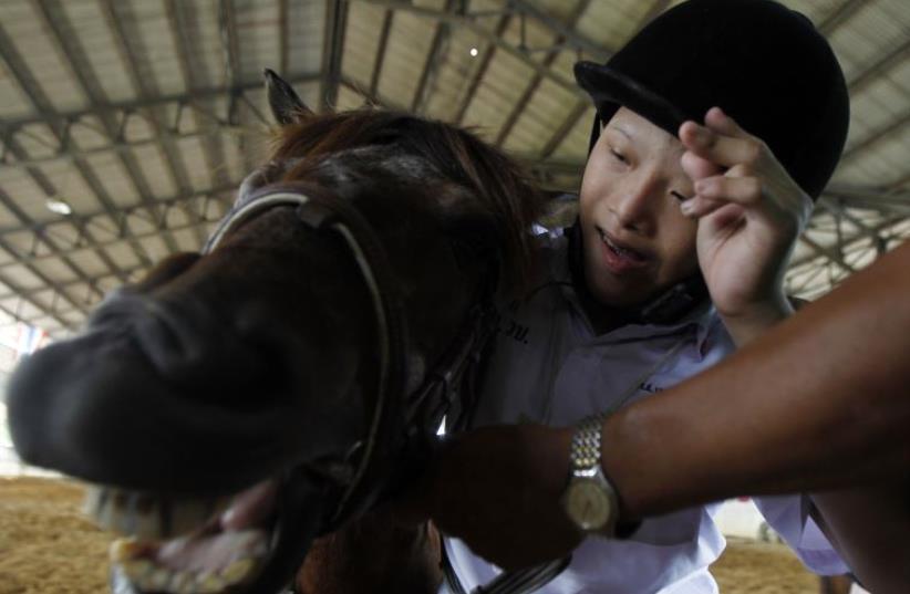 An autistic child plays with a horse during the Horse Therapy Special Children program at the Mounted Police Sub-Division in Bangkok (photo credit: REUTERS)