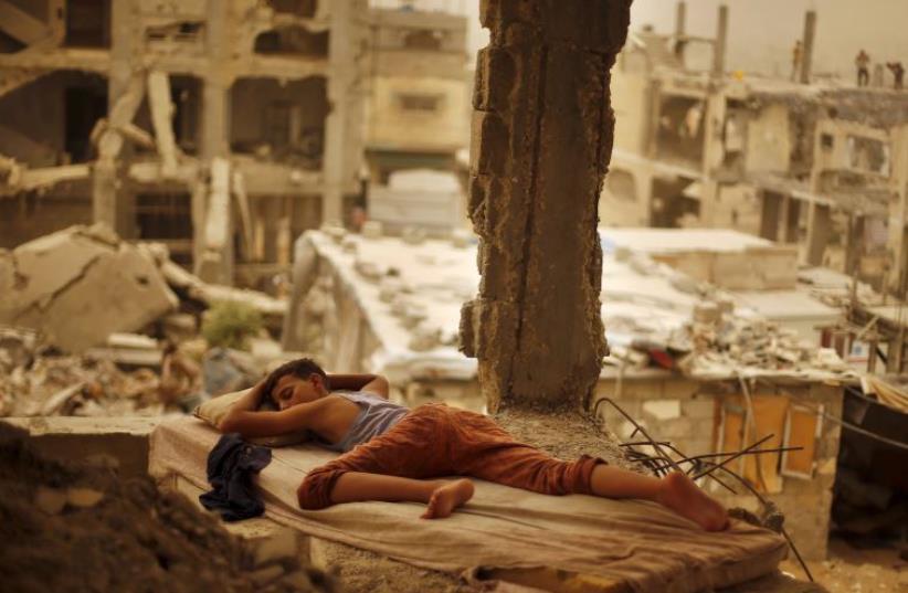 A Palestinian boy sleeps on a mattress inside the remains of his family's house that witnesses said was destroyed by Israeli shelling during Operation Protective Edge (photo credit: REUTERS)