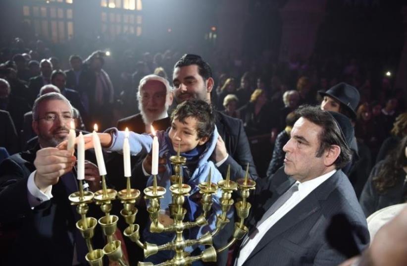 The families of the victims of the Hyper Cacher terrorist attack (Philippe Braham, Yohan Cohen, Yoav Hattab, and François-Michel Saada) in Paris last year light the Hanukka candles at the "Let There Be Light" - Unity Gathering in Paris (photo credit: ISRAEL BARDUGO)