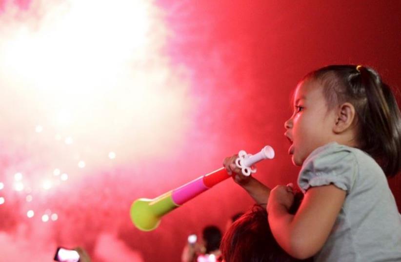 A girl blows a party horn at midnight during New Year celebrations in Manila, Philippines (photo credit: REUTERS)